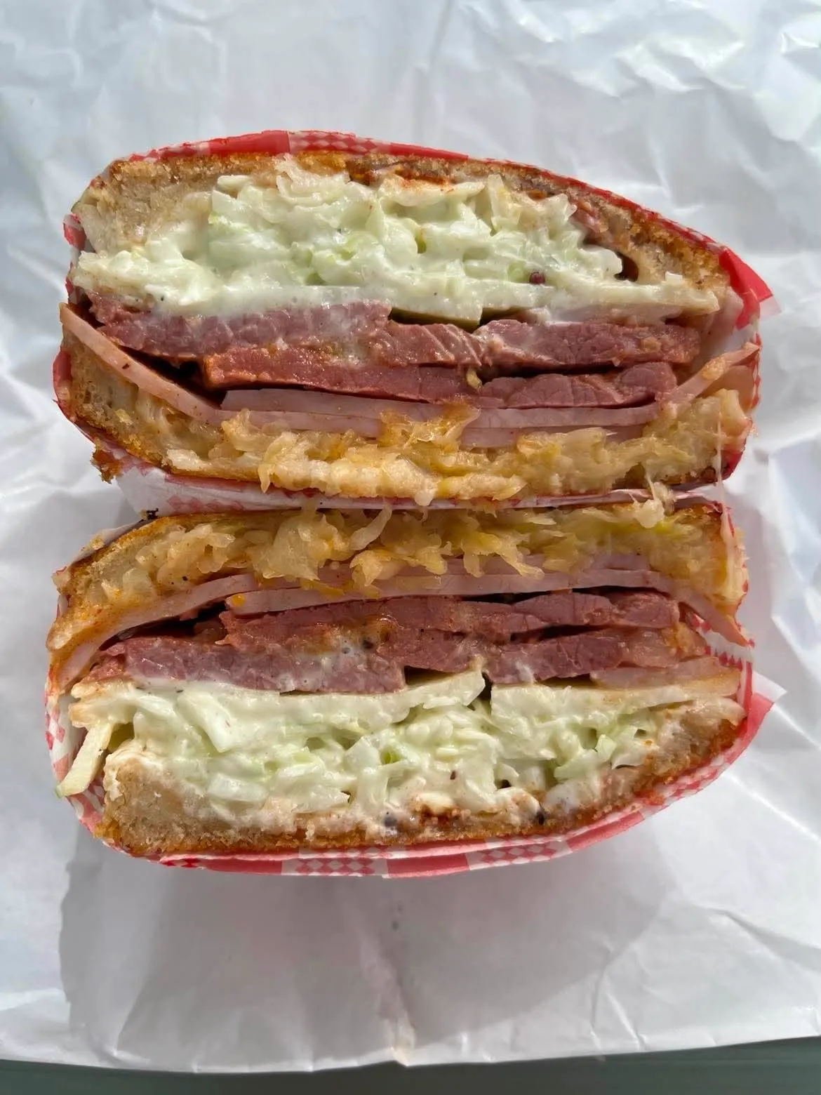 A Reuben deli sandwich cut in half with layers of corned beef, ham, sauerkraut, cheese and cabbage slaw